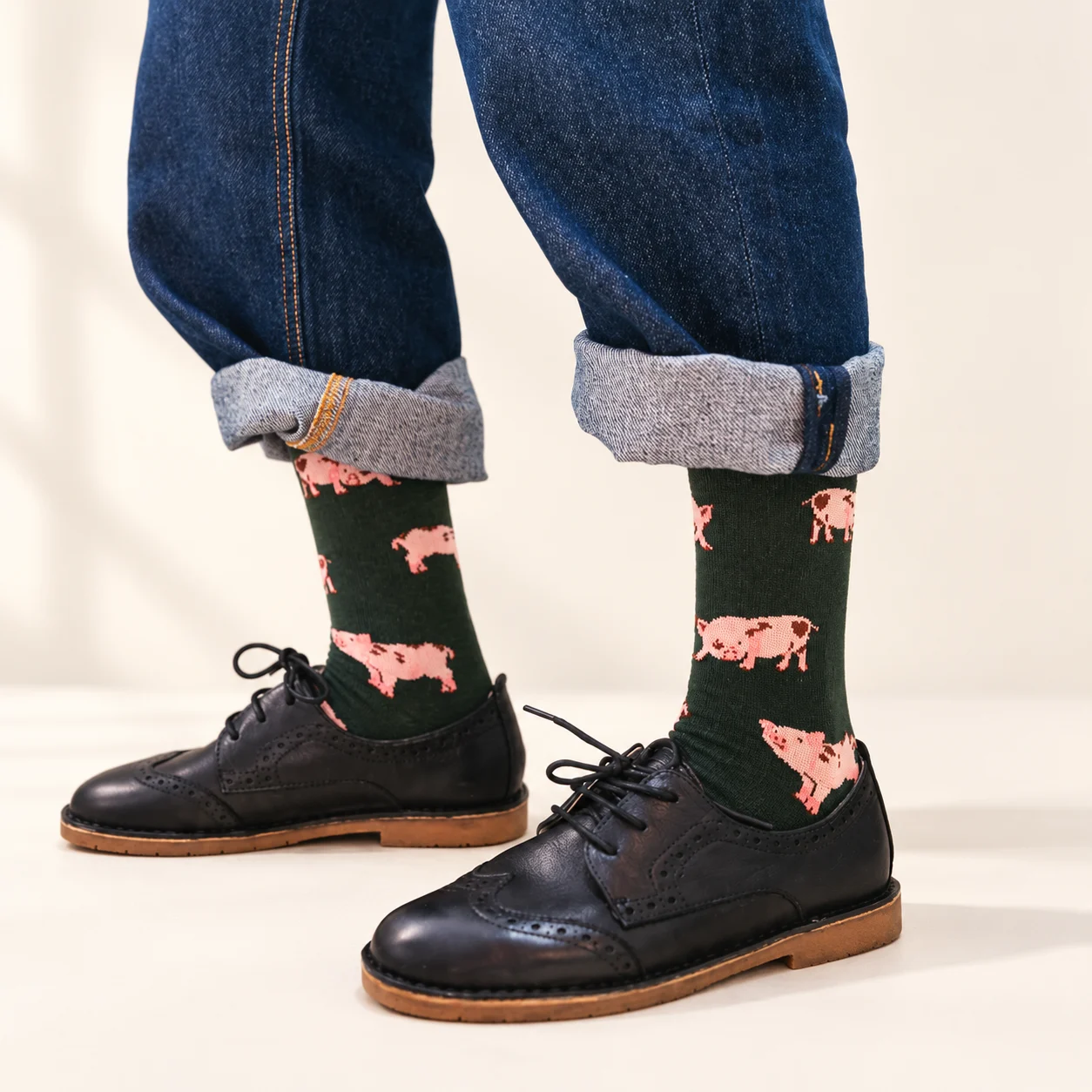 Dark green Piggy Socks with pink pig motifs, shown with cuffed jeans and black lace-up shoes